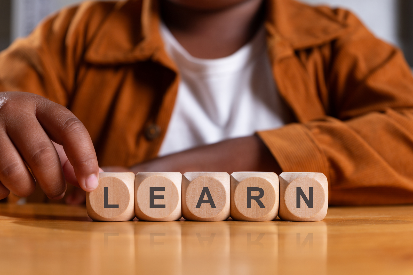 Child's hand touching wooden blocks spelling LEARN